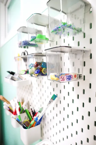 Nahaufname eines Lochbrettes mit Kisten und Kästchen mit therapeutischen Zubehör wie Würfel, Stifte, Murmeln.